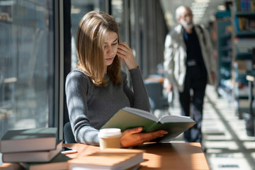 beautiful young girl schoolgirl reads book in school bookstore on sunny day