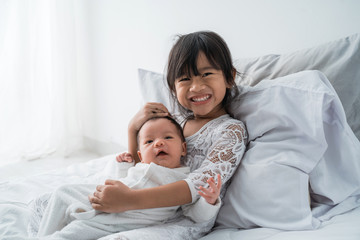 smiling happy girl sibling infant lying on bed play together