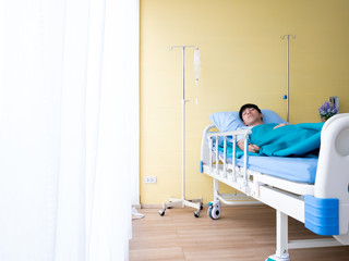 20s 30s Asian patient young man asleep on bed for recovery body from illness symptom in yellow VIP emergency room hospital and beautiful flower from caregiver and visitor with white curtain copy space