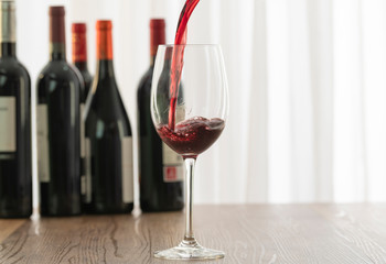 Detail of a glass cup filled with red wine with five bottles of wine in the background blurred on a wooden table. Concept of celebration.