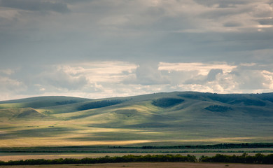 Fototapeta na wymiar Grass hills covered with trees in steppe under spectacular clouds sky during sunset at Khakassia, Siberia, Russia.
