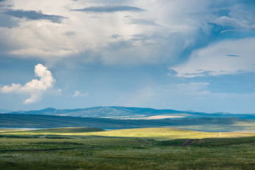 Panoramic landscape with steppe covered with green and yellow grass under blue sky with heavy clouds at Khakassia, Siberia, Russia.