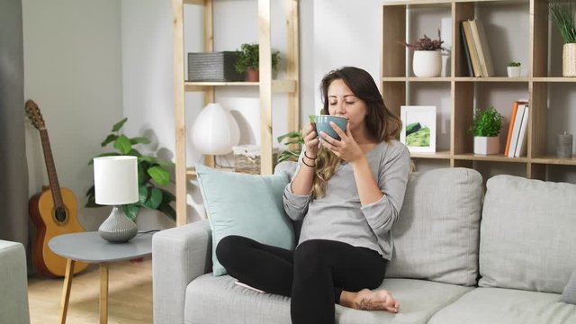 Young woman drinks from a large cup in a cozy living room