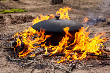 Closeup of cauldron licked by flames on open fire. The process of cooking in the forest.