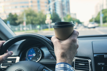 Elderly Businessman drinking coffee from paper cup while driving a car on the highway. Selective focus