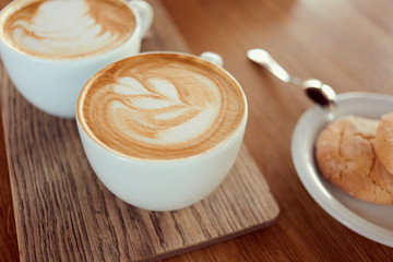 Morning wake up drink. Cups of cappuccino with cookies standing on wooden table.