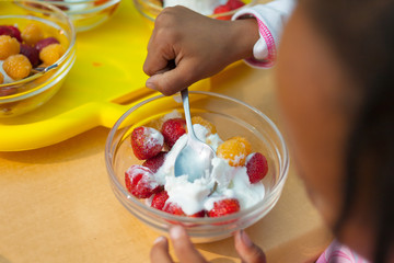 Little girl eating vanilla ice cream with fruits in a hot summer day