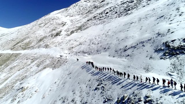 climbers group in chain goes up snowy mountain slope to top. Drone aerial shot