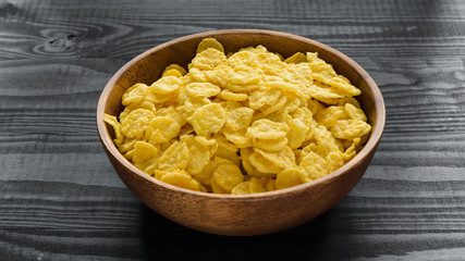 wooden bowl with cornflakes on a dark wooden background