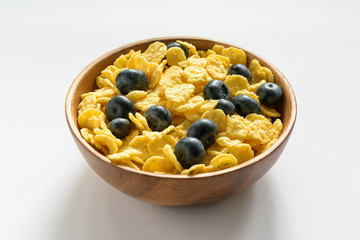 wooden bowl with cornflakes and blueberries on a light background