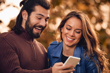 Young couple using cellphone in autumn colored park.