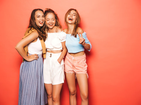 Three young beautiful smiling hipster girls in trendy summer clothes. Sexy carefree women posing near pink wall in studio. Positive models going crazy and having fun