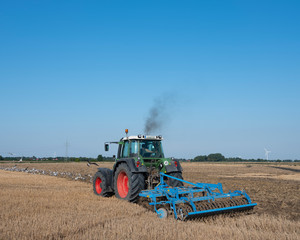 Fototapeta premium tractor with plow in summer field under blue sky near aurich in germany