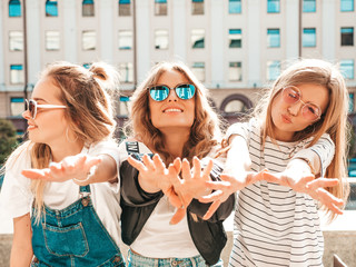 Portrait of three young beautiful smiling hipster girls in trendy summer clothes. Sexy carefree women posing on the street background.Positive models having fun in sunglasses.show their palms