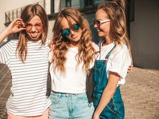 Portrait of three young beautiful smiling hipster girls in trendy summer clothes. Sexy carefree women posing the street.Positive models having fun in sunglasses.Hugging and showing tongue