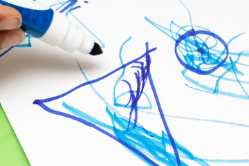 A closeup view of a child drawing colorful pictures with a blue felt tip marker pen on white paper, preschool art and education, learning and development of infants.
