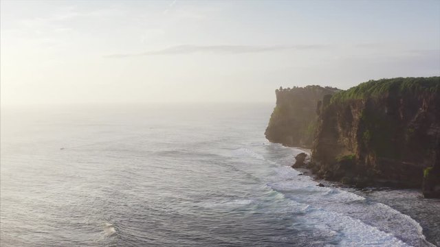 Amazing aerial view of high cliffs above blue ocean. Silhouette of Uluwatu temple on the cliff top. Bali, Indonesia
