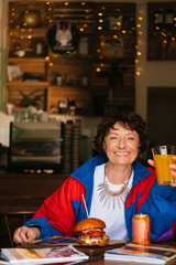 Fototapeta na wymiar Portrait of a happy beautiful fashionable grandmother sitting in a cafe in stylish bright clothes