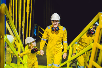 Young man and a little boy are both in a yellow work uniform, glasses, and helmet in an industrial...