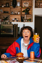 Fototapeta na wymiar Portrait of a happy beautiful fashionable grandmother sitting in a cafe in stylish bright clothes