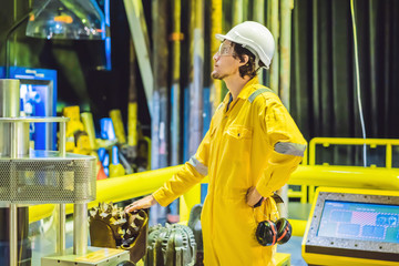 Young man in a yellow work uniform, glasses and helmet in industrial environment,oil Platform or...