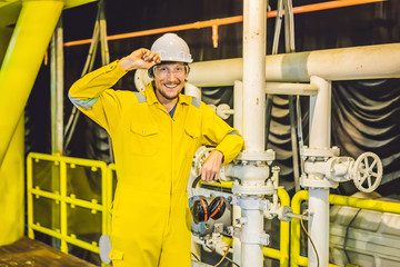 Young man in a yellow work uniform, glasses and helmet in industrial environment,oil Platform or...