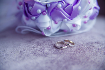 Silver wedding rings and a wedding bouquet on a lilac background