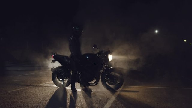 Silhouette of rider and motorcycle in backlight at night. Smoke from tires around  motorcycle rider.  Night racing. Need for speed.