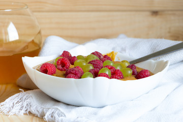 Flaxseed porridge with grapes and raspberries in white bowl with spoon. Honey in glass jar near.