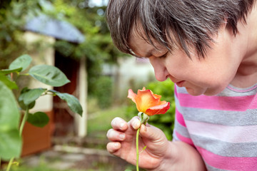 Frau mit geistiger Behinderung riecht an einer Rose im Garten, Bewusstsein und Selbstbestimmung