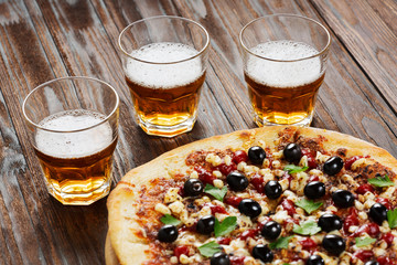 Pizza with olives and herbs and beer on a wooden table