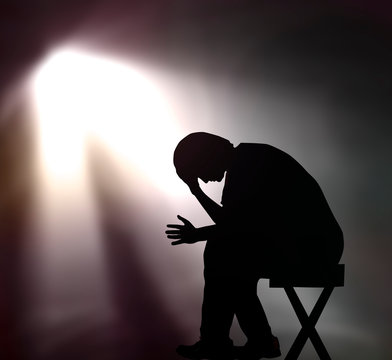 Silhouette of sad man sitting on chair in dark with spotlight showing depression or grief concept