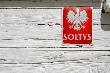 Information board with coat of arms of Poland and VILLAGE MAYOR (polish: SOLTYS) inscription on the white wall. Name given to the elected head of a rural subdivision (village)