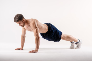 young man with a beard of a sports physique doing push-ups from the floor on a white isolated background, sportsman goes in for sports