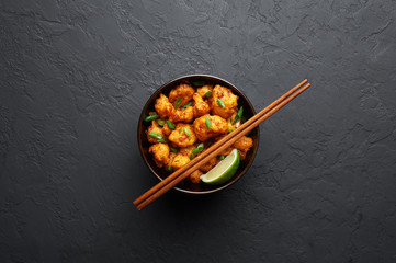Gobi Manchurian in bowl at black concrete background. Gobi Manchurian is Indian Chinese cuisine dish with cauliflower, tomatoes, onion, soy sauce. Copy space