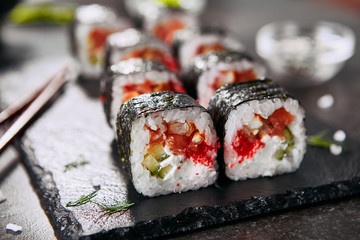 Macro photo of dragon roll with cream cheese, salmon, eel, rice, cucumber, flying fish caviar and nori. Dragon unagi maki rolls with raw red fish and tobiko on natural dark stone background close up