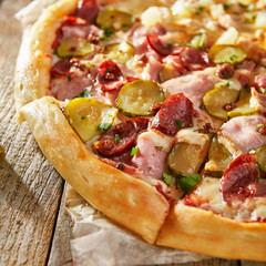 Pizza half with chicken and pineapple on another sausage chopped on boards with vegetables leaves and olives