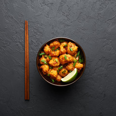Gobi Manchurian in bowl at black concrete background. Gobi Manchurian is Indian Chinese cuisine dish with cauliflower, tomatoes, onion, soy sauce. Copy space
