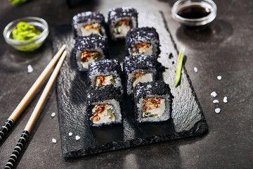 Macro shot of unagi maki rolls with rice, cream cheese, eel, cucumber, flying fish black caviar and nori closeup. Fresh japanese uramaki rolls with tobiko on black slate plate background