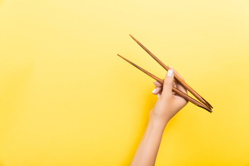 Female hand with chopsticks on yellow background. Traditional asian food with emty space for your design
