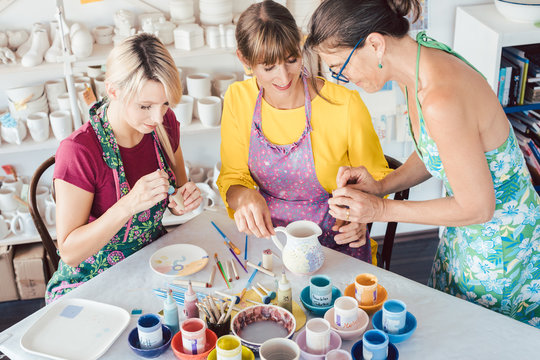 Teacher showing women in workshop how to paint self-made dishes