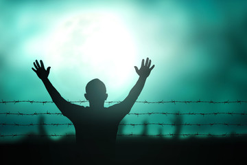 Human right day concept: Silhouette refugee hands raising and barbed wire on night background