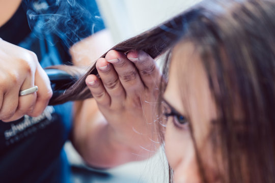 Hairdresser Using Flat Iron On Hair Of Woman Customer