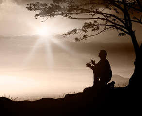 Pray concept: Humble man kneeling to praise and worship God on mountain sunset background