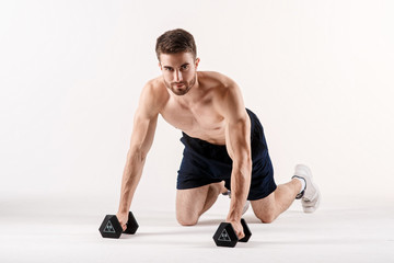 A man on a white isolated background is pushing up on the floor with dumbbells. Bearded bodybuilder athletic