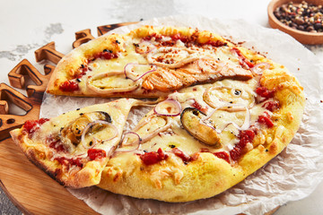 Hot seafood pizza with squid, mussels and fish fillet on wooden plate