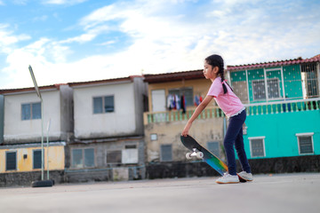 Asian little girl holding skateboard and smile with happiness town and blue sky select focus shallow depth of field