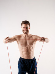 Fototapeta premium Young sporty man with a beard on a white background with gymnastic elastic bands in his hands. training with rubber bands