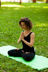 Attractive and tranquil woman sits in lotus position under tree. Yoga and meditation, concentration and relaxation, unity with nature.