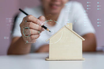 Happy Asian woman using pencil to draw a plan with wooden house piggy bank metaphor planning to saving money for buy the house select focus shallow depth of field